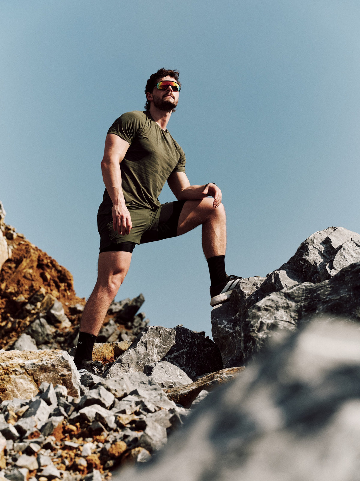 Centric athlete in olive activewear standing on mountain rocks